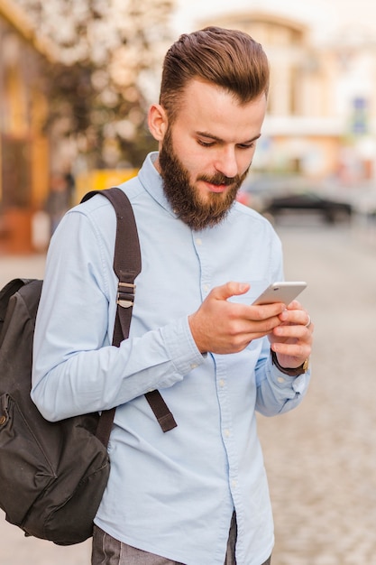 Brodaty młody człowiek używa smartphone