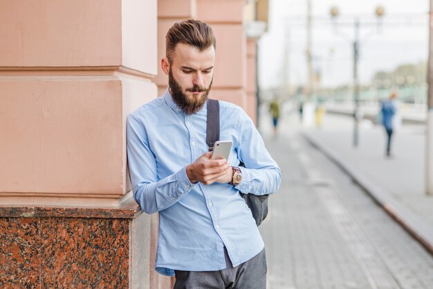 Brodaty młody człowiek używa telefon komórkowego przy outdoors