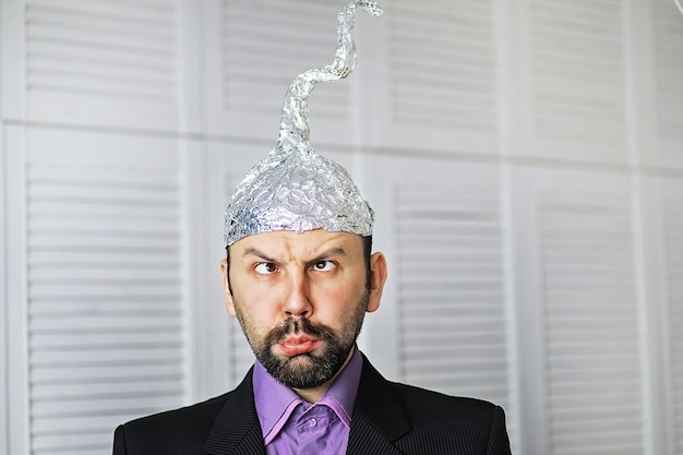 Brodaty zabawny mężczyzna w czapce z folii aluminiowej. fobie koncepcyjne. teoria spiskowa. spisek. niepoczytalność.