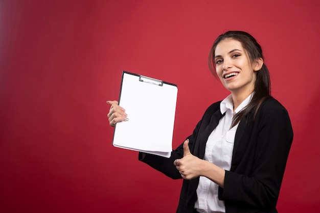 Brunetka bizneswoman trzyma schowek i daje kciuki do góry.