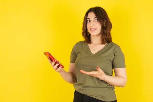 Brunetka kobieta model stojący i za pomocą telefonu komórkowego przed żółtą ścianą.