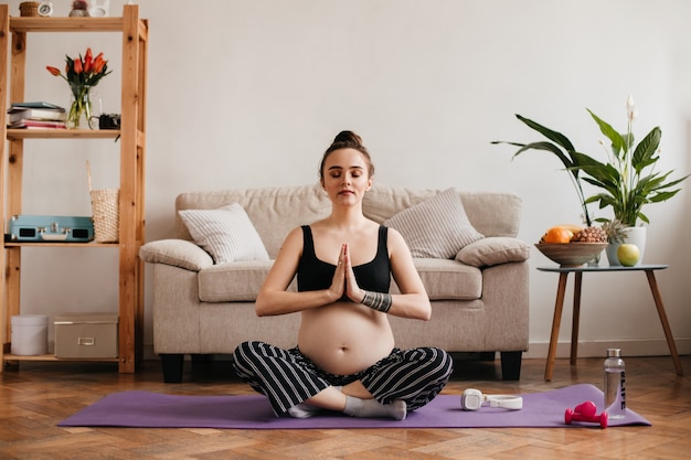 Brunetka kobieta w ciąży medytuje i robi joga w salonie