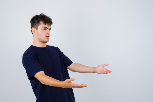 Brunetka mężczyzna robi gest pytający, stojąc bokiem w ciemnym t-shircie i patrząc zdziwiony.