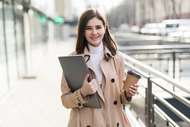 Brunetka model w przypadkowych ubraniach zostaje z laptopem na zewnątrz