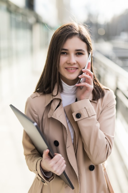 Brunetka model z laptopem w dłoniach ma połączenie telefoniczne w swoim telefonie