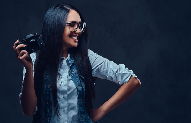 Brunetka podróżniczka z plecakiem trzyma kompaktowy aparat fotograficzny.