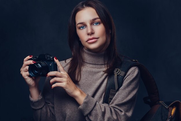 Brunetka podróżniczka z plecakiem trzyma kompaktowy aparat fotograficzny.