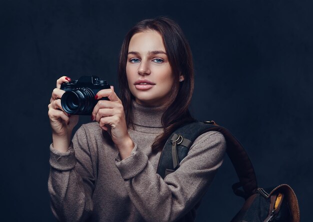 Brunetka podróżniczka z plecakiem trzyma kompaktowy aparat fotograficzny.