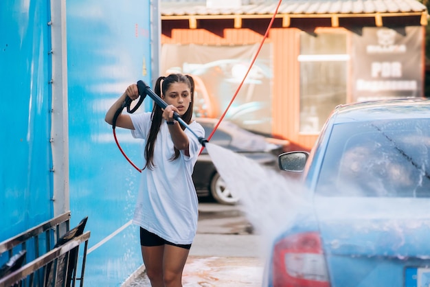 Brunetka z węża wysokociśnieniowego myje auto na myjni samochodowej