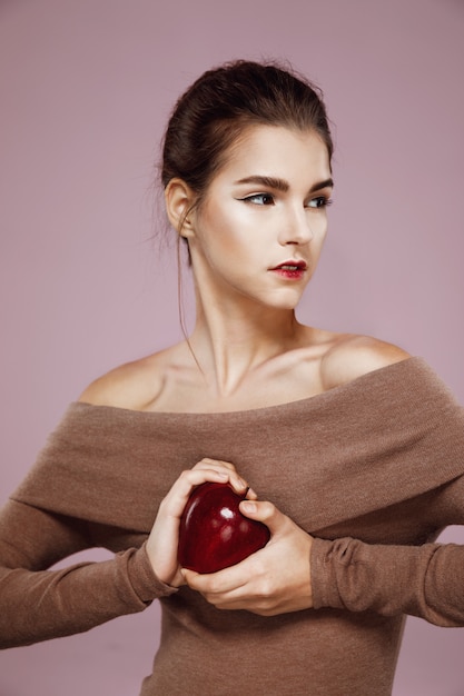 Brutalna młoda kobieta trzyma dużego czerwonego jabłka w rękach na menchiach