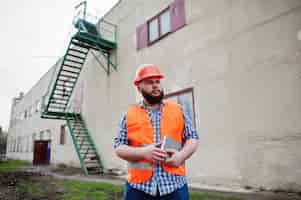 Bezpłatne zdjęcie brutalny pracownik brody mężczyzna garnitur pracownik budowlany w pomarańczowym kasku bezpieczeństwa przebywa w pobliżu dużych schodów przemysłowych