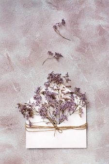Bukiet suszonych kwiatów w lekkiej kopercie przewiązanej liną na teksturowanym tle. pozdrowienie romantyczne karty. widok z góry i z pionu