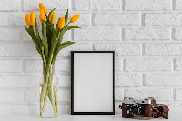 Bezpłatne zdjęcie bukiet tulipanów w przezroczystym wazonie z pustą ramką i aparatem