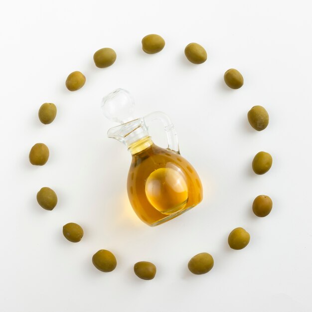 Butelka oliwy z oliwek otoczona zielonymi oliwkami