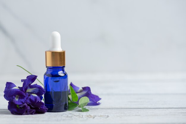 Butelka serum z olejkiem Butterfly Pea Flower nakładana na białą drewnianą podłogę