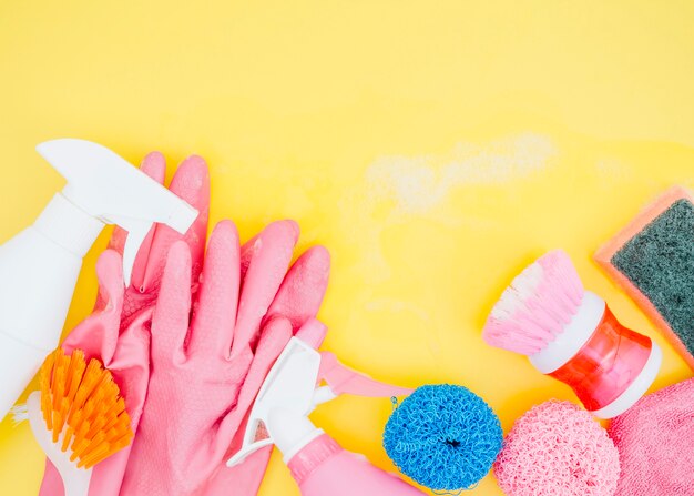 Butelka z rozpylaczem; szczotka; gąbka i różowe rękawiczki na żółtym tle