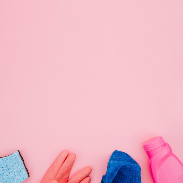 Butelki na detergenty; rękawiczki; niebieska serwetka i gąbki na różowym tle