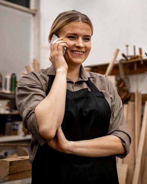 Bezpłatne zdjęcie buźka stolarz kobieta za pomocą smartfona w pracy