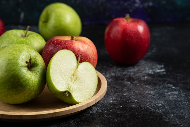 Całe i pokrojone zielone i czerwone jabłka na drewnianym talerzu.