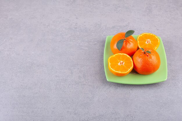 Całe pomarańczowe owoce z pokrojonymi w plasterki mandarynkami umieszczone na zielonym talerzu.