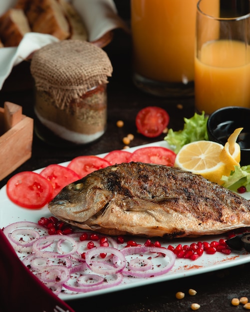 Bezpłatne zdjęcie całe ryby grillowane i podawane z pomidorem, cytryną i cebulą.