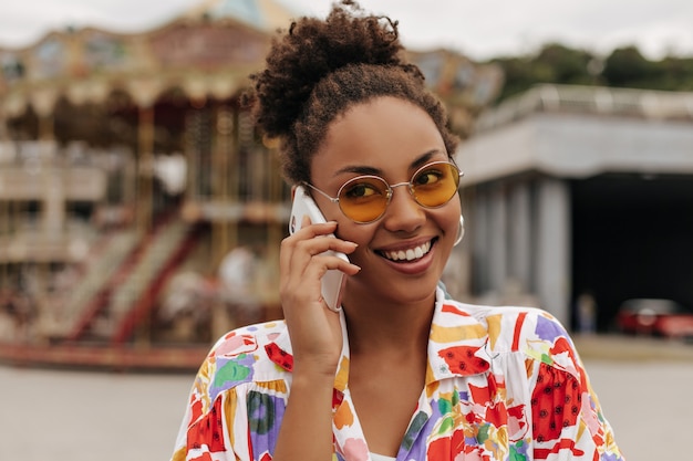 Całkiem atrakcyjna młoda kobieta w pomarańczowych okularach przeciwsłonecznych rozmawia przez telefon