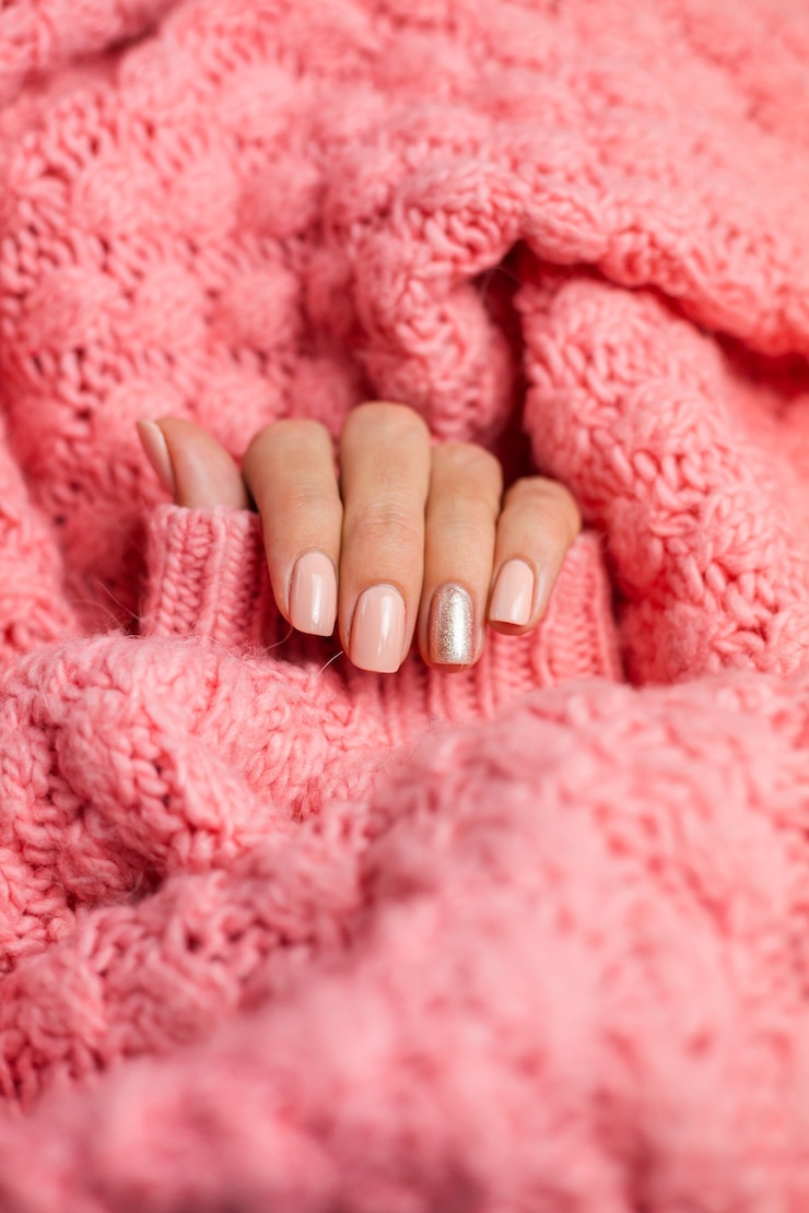 Bezpłatny plik Zdjęcie całkiem cielisty manicure w kolorze cielistym, błyszczącym złotym jednym palcem, na tle dzianinowej poduszki z różowej wełny