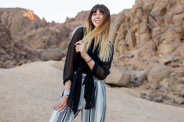 Całkiem uśmiechnięta modna dziewczyna pozuje na wydmach egipskiej pustyni.