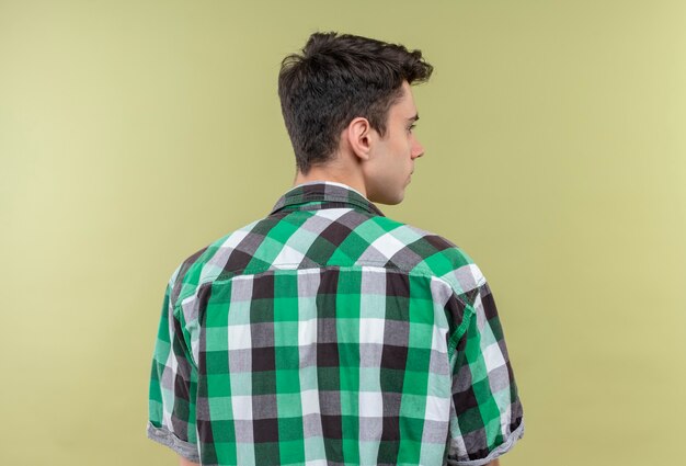 Bezpłatne zdjęcie caucasion młody człowiek ubrany w zieloną koszulę stojąc z powrotem na izolowanych zielonej ścianie