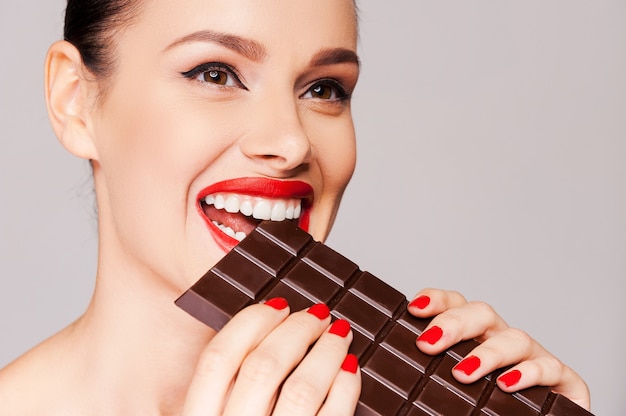 Chcąc, żeby czekolada była owocem. zbliżenie pięknych kobiet trzymających palec na czerwonych ustach, stojąc na szarym tle