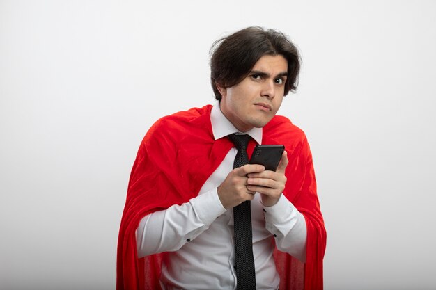 Chciwy młody superbohater facet patrząc na kamery na sobie krawat trzymając telefon na białym tle