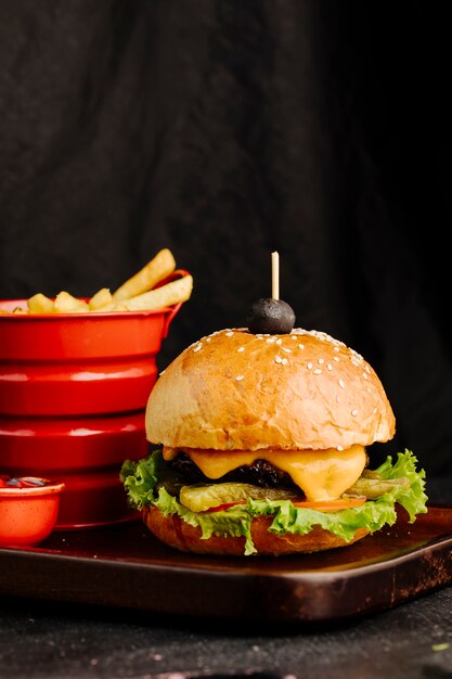 Cheeseburger w bułce z frytkami w czerwonym pojemniku.
