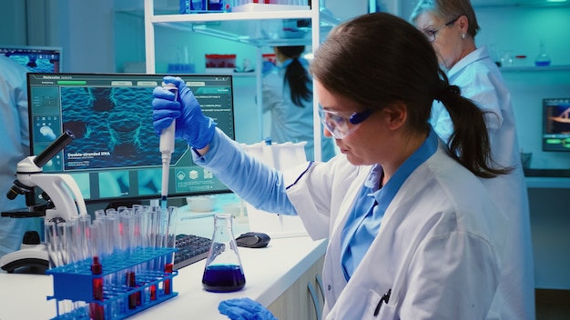 Chemik wlewający płyn do probówki z mikropipetą w nowocześnie wyposażonym laboratorium