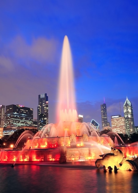 Chicago skyline z drapaczami chmur i fontanną Buckingham w Grant Park o zmierzchu, oświetlone kolorowymi światłami.