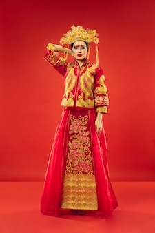 Chiński tradycyjny pełen wdzięku kobieta w studio na czerwonym tle. piękna dziewczyna w stroju ludowym. chiński nowy rok, elegancja, wdzięk, wykonawca, wydajność, taniec, aktorka, koncepcja emocji
