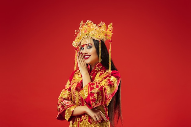 Chiński tradycyjny pełen wdzięku kobieta w studio na czerwonym tle. Piękna dziewczyna w stroju ludowym. Chiński Nowy Rok, elegancja, wdzięk, wykonawca, wydajność, taniec, aktorka, koncepcja ubioru