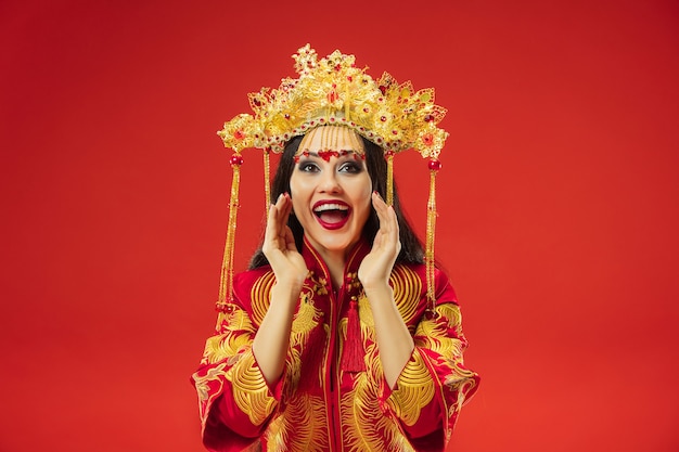 Bezpłatne zdjęcie chiński tradycyjny pełen wdzięku kobieta w studio na czerwonym tle. piękna dziewczyna w stroju ludowym. chiński nowy rok, elegancja, wdzięk, wykonawca, wydajność, taniec, aktorka, koncepcja ubioru
