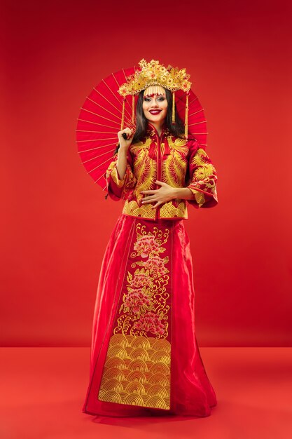 Chiński tradycyjny pełen wdzięku kobieta w studio na czerwonym tle.