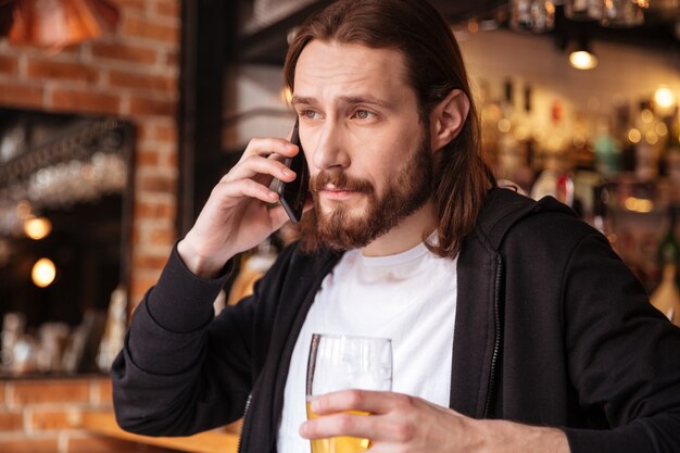 Chłodny brodaty mężczyzna rozmawia przez telefon w pobliżu baru