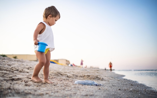 Chłopiec bawiący się zabawkami na plaży budujący koraliki i wieżyczki uśmiechający się do kogoś za kulisami na letnie wakacje