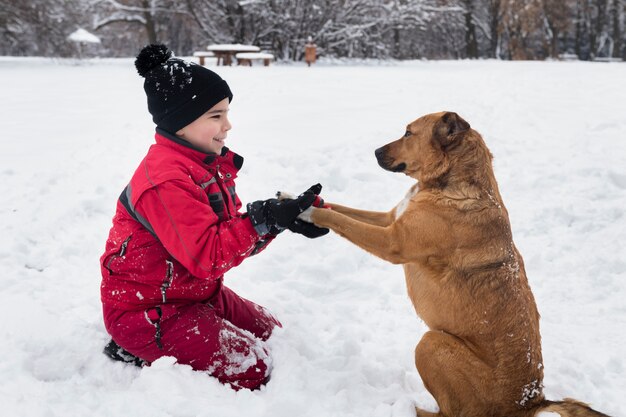 Chłopiec bawić się z brązu psem na śniegu w zimie