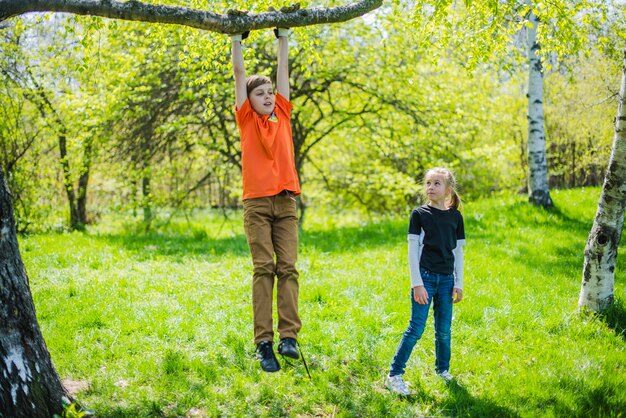 Chłopiec gra na gałęzi, podczas gdy jego siostra patrzy na niego