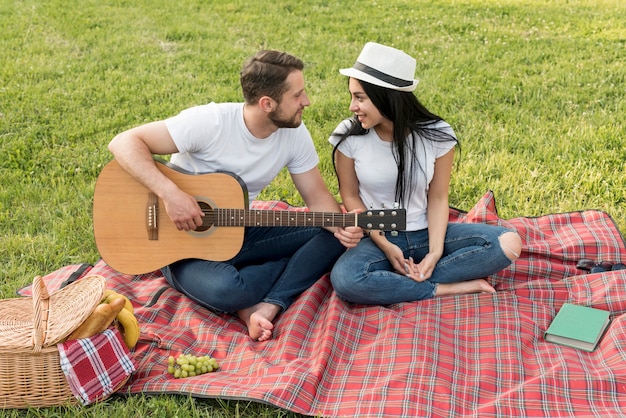 Chłopiec gra na gitarze dla swojej dziewczyny na koc piknikowy