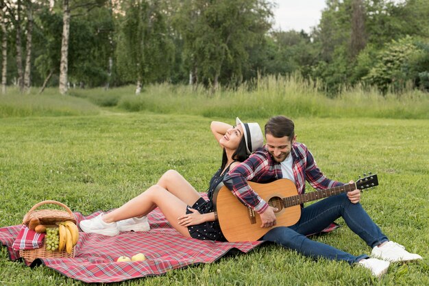 Chłopiec gra na gitarze dla swojej dziewczyny na koc piknikowy