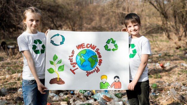 Chłopiec i dziewczynka trzymający plakat w obronie ekologii przy zbiórce plastikowych śmieci