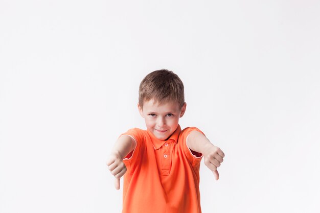 Chłopiec jest ubranym pomarańczową koszulkę pokazuje niechęć gest przeciw białemu tłu
