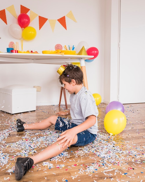Chłopiec obsiadanie na podłogowym bawić się z papierowymi confetti po tym jak partyjny świętowanie