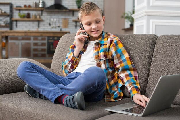 Chłopiec używa laptop na leżance i robi rozmowie telefonicza