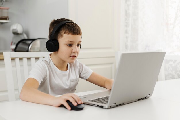 Chłopiec w domu, grając na laptopie i nosząc słuchawki