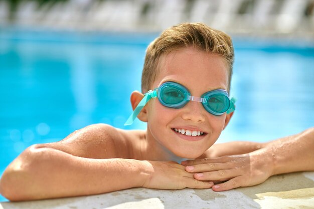 Chłopiec w okularach pływackich w basenie patrząc na kamerę